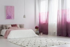 Gradient curtains in bright bedroom with patterned carpet and pink painting on the wall above bed